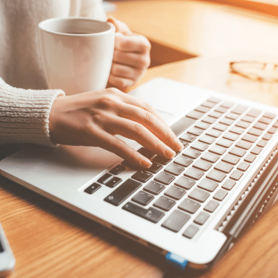 Person working on a laptop, holding a cup of coffee, representing cary smiles new website
