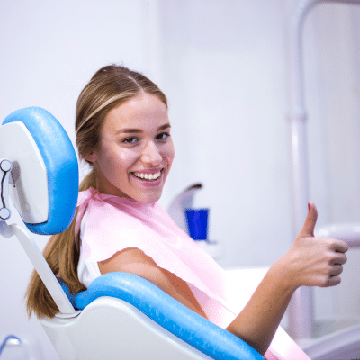 A woman sitting in a dental chair giving a thumbs up, representing importance of dental check-ups