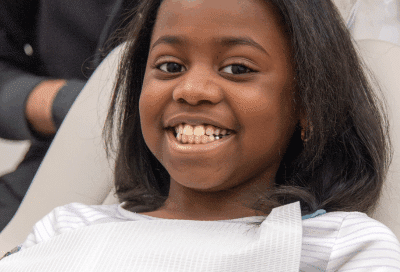 Little girl smiling while sitting in dental chair at cary smiles, representing clear aligner maintenance