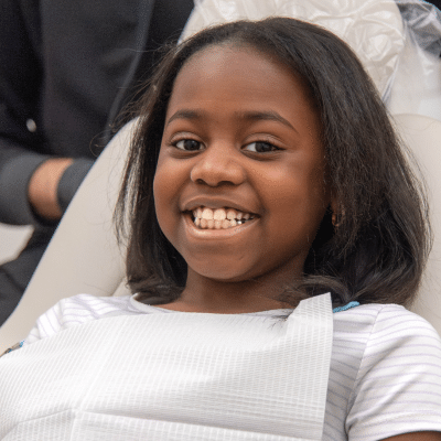 Little girl smiling while sitting in dental chair at cary smiles, representing clear aligner maintenance