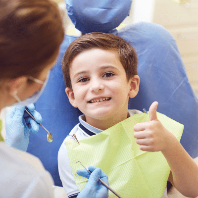 Child at dentist giving thumbs up, representing how to teach kids good dental habits